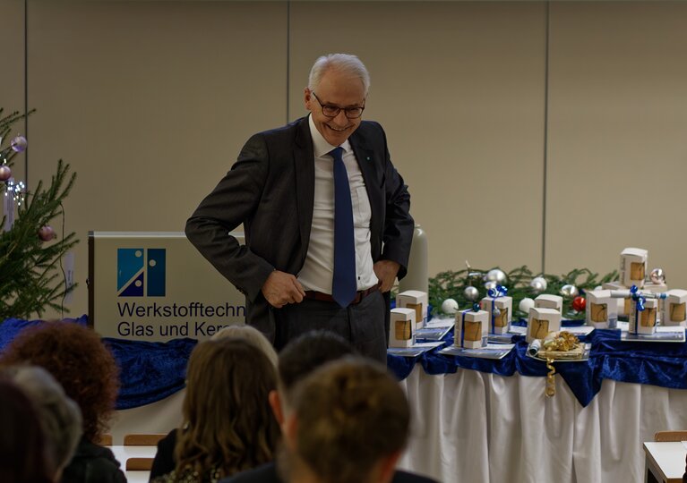 Der Präsident der Hochschule steht vorne an der Bühne. Abschlussgeschenke im Hintergrund. 