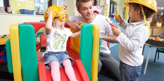 Ein Erzieher spielend mit zwei Kindern in der Kita.