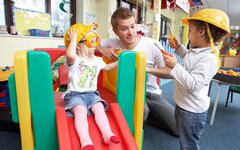 Ein Erzieher spielend mit zwei Kindern in der Kita.