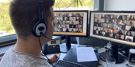 Mann mit Headset sitzt vor zwei Bildschirmen und nimmt an einer Online-Konferenz teil