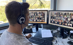 Mann mit Headset sitzt vor zwei Bildschirmen und nimmt an einer Online-Konferenz teil
