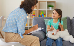 Happy little girl telling story to child psychologist during therapy session in cozy modern office