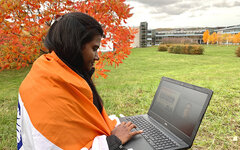 Austauschstudentin sitzt mit ihrem Laptop vor dem RheinAhrCampus auf der Wiese