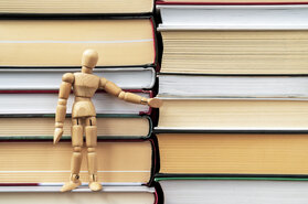 Wooden mannequin standing on the stack of books