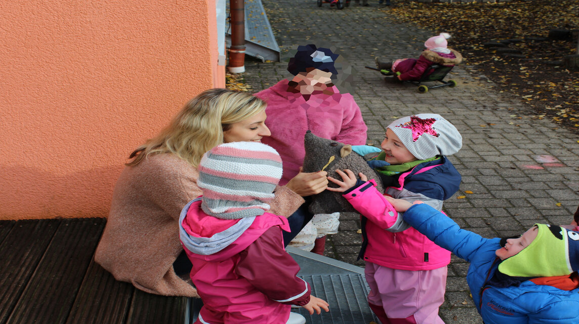 Erzieherin und Kita-Kinder zusammen mit dem Maskottchen Ebbi