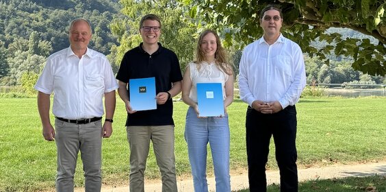 Eine Gruppe von vier Personen steht auf einer Wiese. Die Preisträgerin und der Preisträger halten ihre Urkunde in der Hand. 