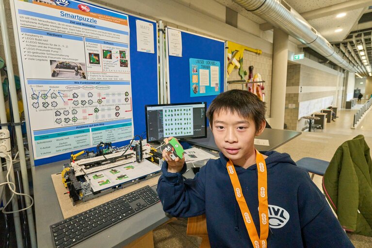 Ein Junge mit einem Puzzleteil in der Hand und einem PC im Hintergrund.