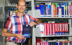 Professor Neuhäuser mit seinem Buch in der Bibliothek der Hochschule.