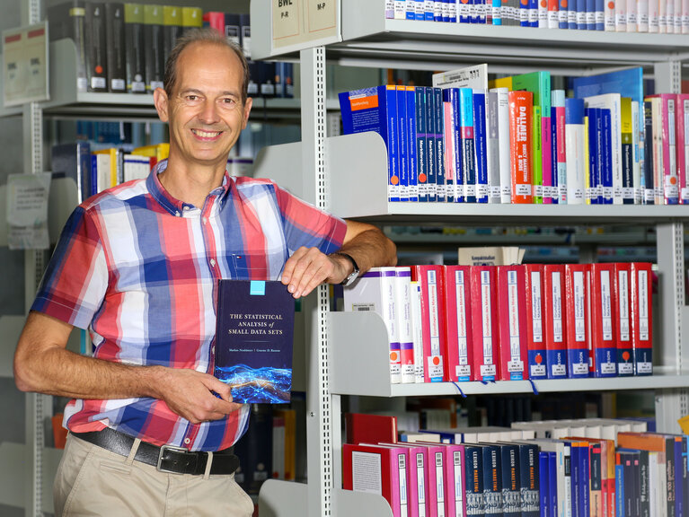 Professor Neuhäuser mit seinem Buch in der Bibliothek der Hochschule.